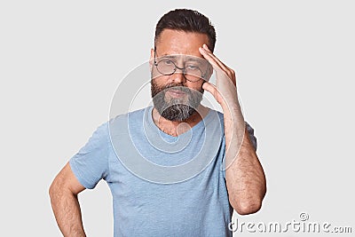 Close up portrait of handsome middle aged man. Bearded male in grey clothes and glasses thinking and looking aside, keeps hand on Stock Photo