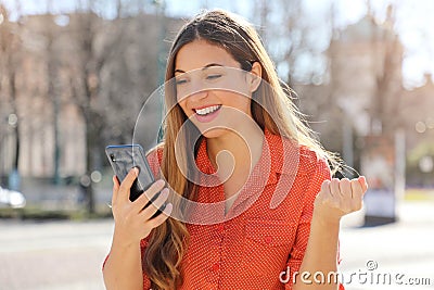 Close up portrait of happy excited satisfied girl reading good news on mobile phone and celebrating with fist up in city street Stock Photo