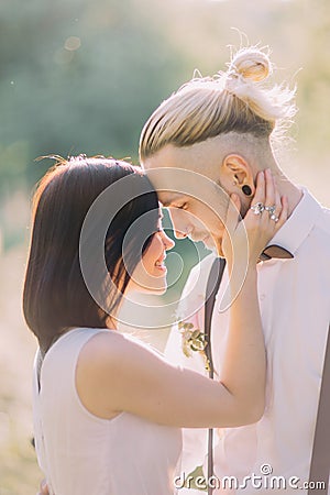 Close-up portrait of the happy and smiling newlyweds in the sunny forest. The bride in the white dress is petting the Stock Photo