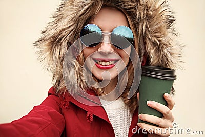 Close up portrait of happy smiling woman stretching hand for taking selfie with coffee cup wearing red jacket Stock Photo