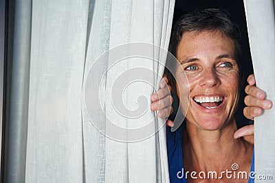 Close up happy woman opening curtain and looking through window Stock Photo