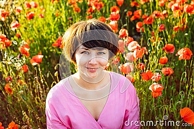 Close up portrait of happy young woman in a pink dress relaxing in red poppies flowers meadow in sunset light. A simple pleasure Stock Photo