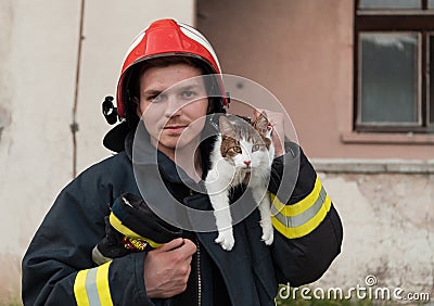 Close-up portrait of heroic fireman in protective suit and red helmet holds saved cat in his arms. Firefighter in fire Stock Photo