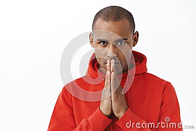 Close-up portrait of hopeful young determined african american man in red hoodie, praying, awaiting important news Stock Photo