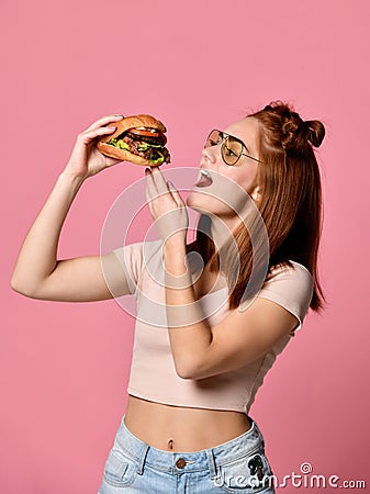 Close up portrait of a hungry young woman eating burger isolated over pink background Stock Photo