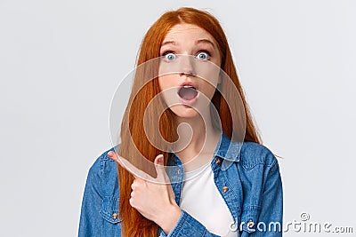 Close-up portrait impressed shook and speechless pretty redhead female student, teenager pointing upper left corner drop Stock Photo