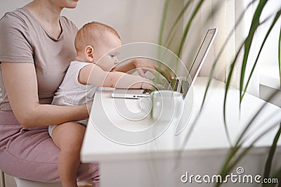 Close up portrait little baby boy funny facial expression sitting on mother`s lap studying laptop. Young mom work from home with Stock Photo