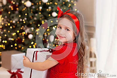 Close-up portrait Little girl in a red dress laughs and enjoys the gift. Little girl opening a magical christmas present at home. Stock Photo