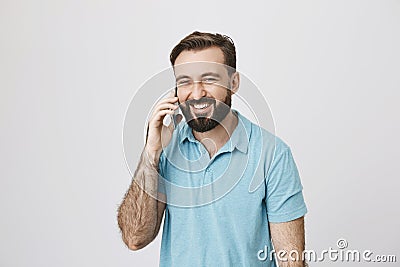 Close up portrait of man with a beard talking on the phone standing near white wall. Coworker rang and told funny story Stock Photo