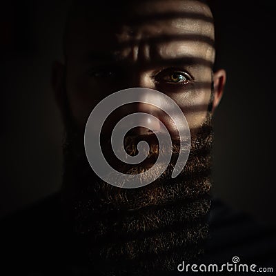 Close-up portrait of middle aged brutal bearded man with expressive eyes and striped shadows on his face Stock Photo