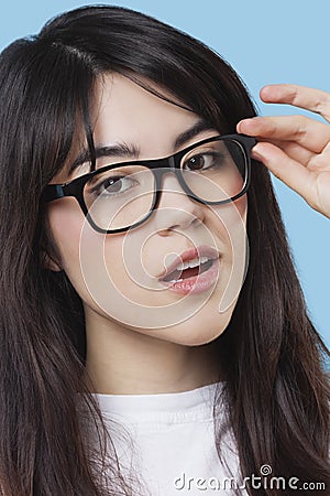 Close-up portrait of mixed race young woman wearing eyeglasses over blue background Stock Photo