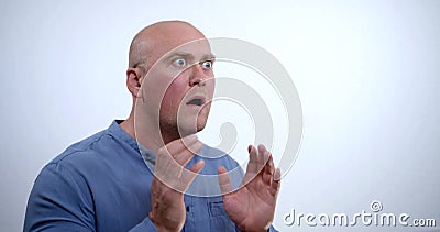 Close-up portrait of a nervous bald middle-aged man in a blue shirt, he sits in the Studio on a white background Stock Photo