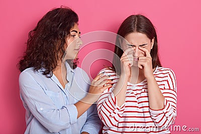 Close up portrait of one teenage girl comforting another after break up, female wearing striped shirt crying in studio, her friend Stock Photo