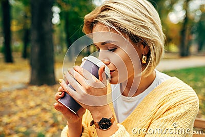 Close-up portrait of pretty young woman drinking coffee at terrace cafetaria in the park. Blonde female in the city street Stock Photo