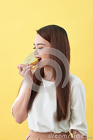 Close up portrait of a satisfied pretty girl eating donuts over yellow background Stock Photo