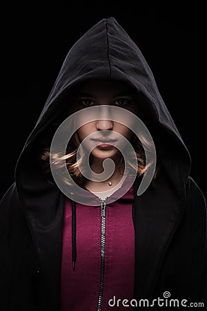 Close-up portrait of a secretive young girl in a deep dark hood on a black background. The concept of secrecy of secrets Stock Photo