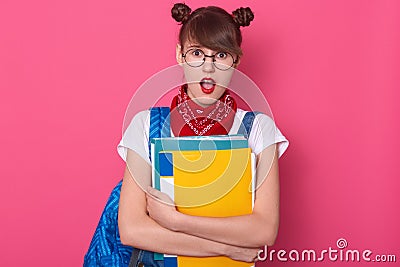 Close up portrait of student with two funny bunches, wearing white t shirt, denim overalls, red bandana and rounded eyewear, Stock Photo