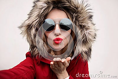 Close up portrait of stylish cool woman blowing red lips sending sweet air kiss stretching hand for taking selfie Stock Photo