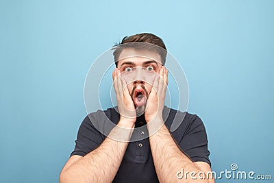 Close-up portrait of a surprised man that took a hand on the face of fear,looks emotionally into the camera on a blue background. Stock Photo