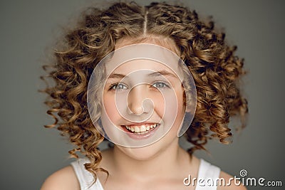Close-up portrait. Teen girl with curly hair smiles beautifully. The vzgyad directs directly into the frame. Gray background. Stock Photo