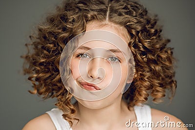 Close-up portrait. A teenage girl with curly hair curled her lips into a tube. The vzgyad directs directly into the frame. Gray Stock Photo