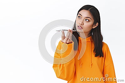 Close-up portrait thoughtful asian girl record voice message, holding smartphone near lips, make notes or talking to Stock Photo