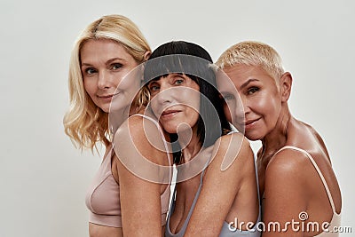 Close up portrait of three beautiful happy mature women in underwear posing together isolated over light background Stock Photo