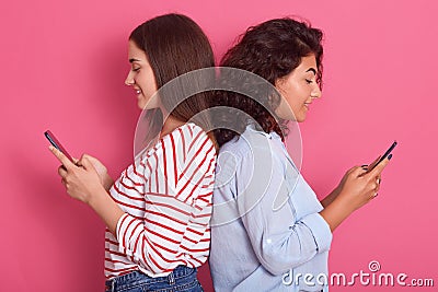 Close up portrait of two cute young women pose together over pink background while standing back to back to each other, Stock Photo