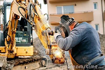 Portrait of welder working on excavator on construction site, reparing and fixing Stock Photo