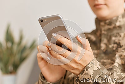 Close up portrait of woman soldier wearing camouflage uniform sitting with smart phone in hands, using cell phone, checking social Stock Photo