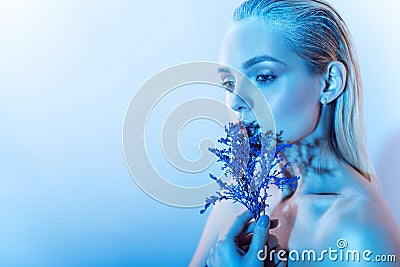 Close up portrait of young beautiful blond model with nude make up, slicked back hair holding a branch of blue flowers Stock Photo