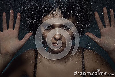 Young beautiful woman with provocative make up and stylish bob haircut standing behind the window with rain drops on it Stock Photo