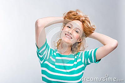 Close-up portrait of a young, beautiful woman with red curly hair in a summer dress with strips of blue in the studio on a gray ba Stock Photo