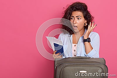 Close up portrait of young brunette woman posing on pink background, being ready to have vacation, stands with suitcase, Stock Photo