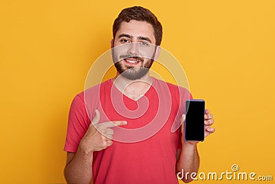 Close up portrait of young happy man in red shirt showing black blank smart phone screen, looking at camera, poses over yellow Stock Photo