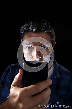 Close up portrait of young man looking intensively to mobile phone screen with blue eyes wide open isolated on black background Stock Photo