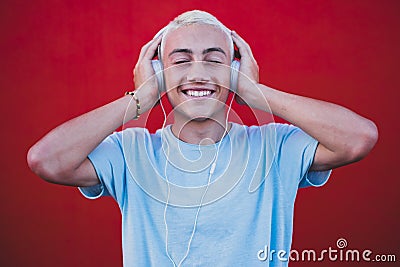 Close up and portrait of young man or millennial hearing and listening music having fun smiling with a red colorful wall at the Stock Photo