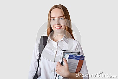 Close up portraitof young girl teenagercarries rucksack, holds colourful folder with papers, has pleasant smile, has lectures in Stock Photo