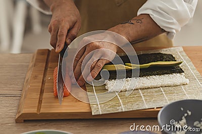 Close up preparing roll sushi at home. Male hands slicing ingredients salmon, cucumber, avocado and cream cheese Stock Photo