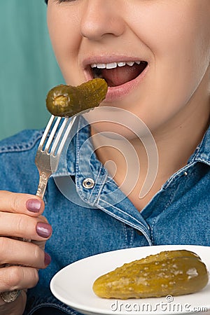 Close-up of a pretty Caucasian woman holding a fork and a plate with pickled cucumber. Front three-quarter view. Low angle view. Stock Photo