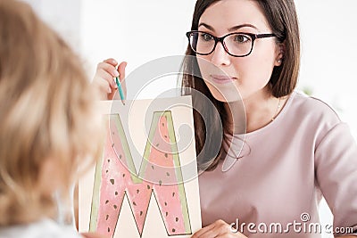 Close-up of a professional child development therapist showing a prop picture of letter `m` to a kid during a meeting. Stock Photo