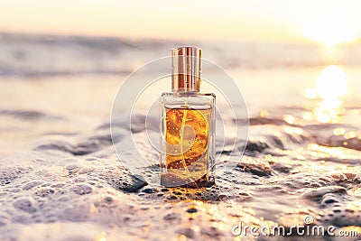 Close up of rectangular glass bottle with golden perfume washed by sea surf. Sunset light in background. Natural Stock Photo