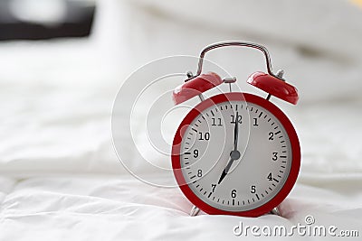 Red alarm clock at 7 oclock on bed Stock Photo