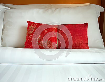 Close up A red Chinese style fabric scatter cushion, backrest pillow, placed in front of double white pillows on the hotel bed, Stock Photo