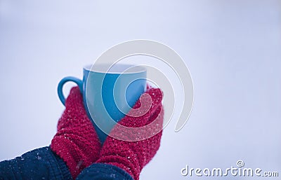 Close-up of a red-gloved hand holding a cup with a hot drink in winter on the snow. Stock Photo