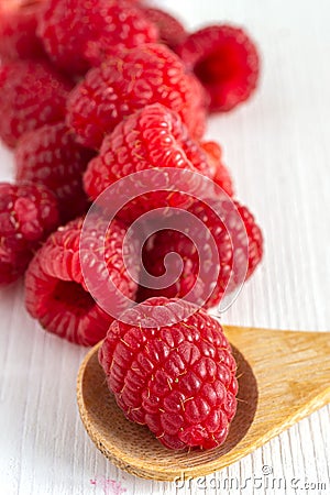 Close-up of red raspberries on white wooden board, with wooden spoon in the foreground and blur in the background. Stock Photo