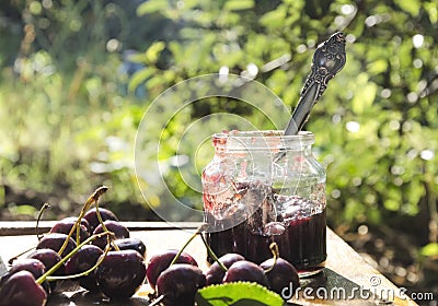 Tasty sweet cherry jam and fresh cherries on the rustic wooden table in the garden Stock Photo