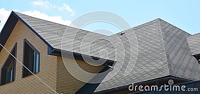 A close-up on a roof problem area covered with asphalt roof shingles and irregular shape window on the wall of the house Stock Photo
