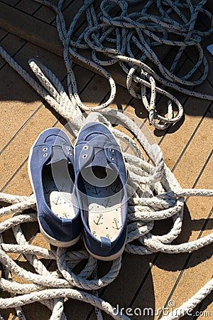 Close-up of a rope with a knotted end tied around a cleat on a wooden pier and shoes with anchors Stock Photo
