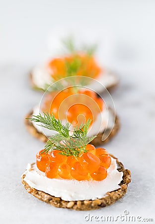 A close up of a row of rustic whole grain crackers topped with cream cheese and caviar and garnished with dill. Stock Photo